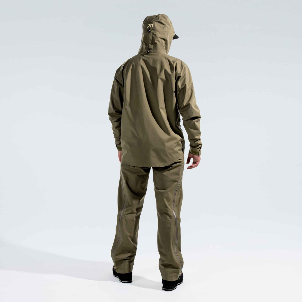 A person viewed from the back wearing an olive green hooded First Lite Borah jacket and matching pants against a light gray studio background.
