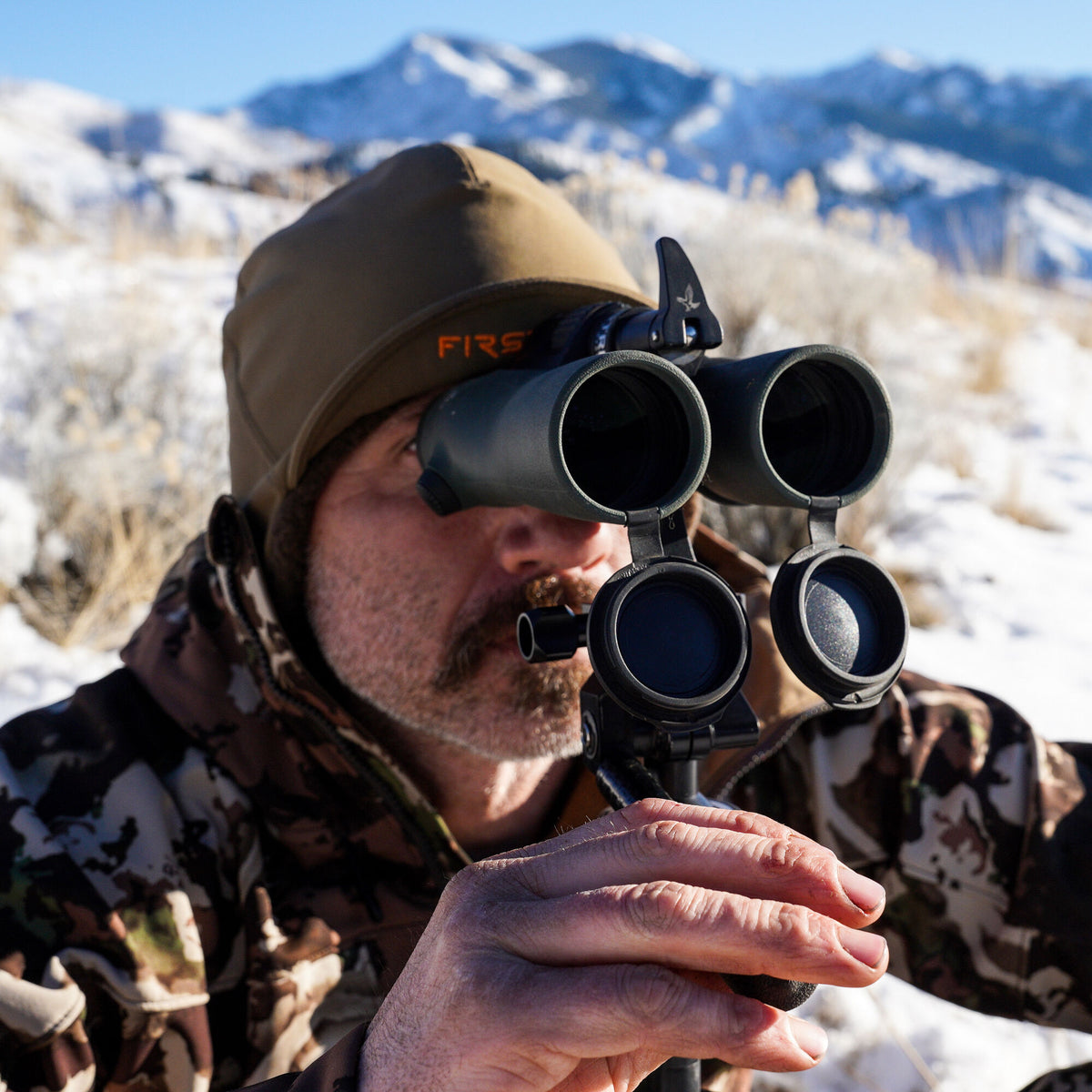 Dark green binoculars with a prominent bird logo, mounted on a stand with open lens caps, used by a man.