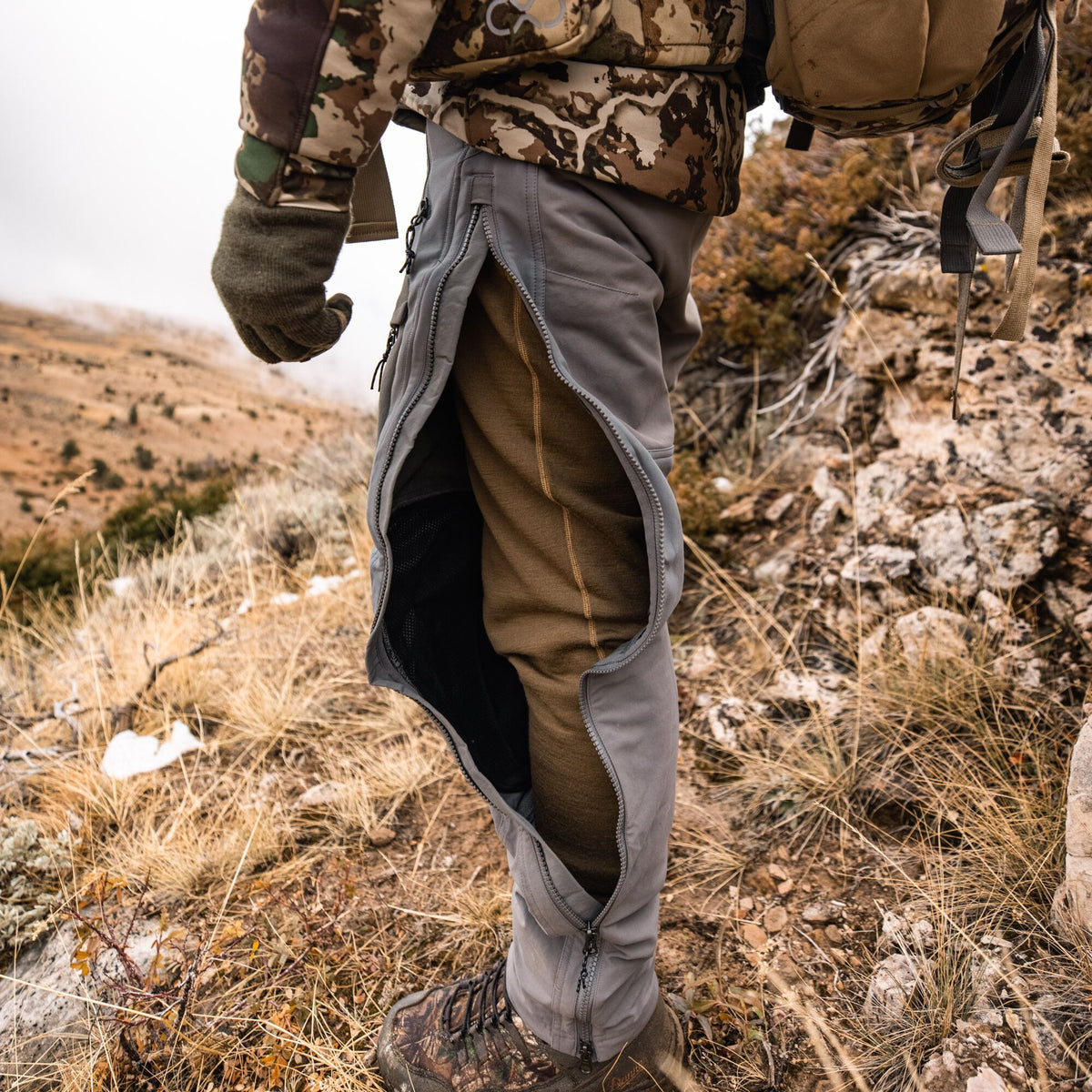Gray hiking pants with a full-length side zipper open to reveal a brown thermal base layer and black mesh lining.