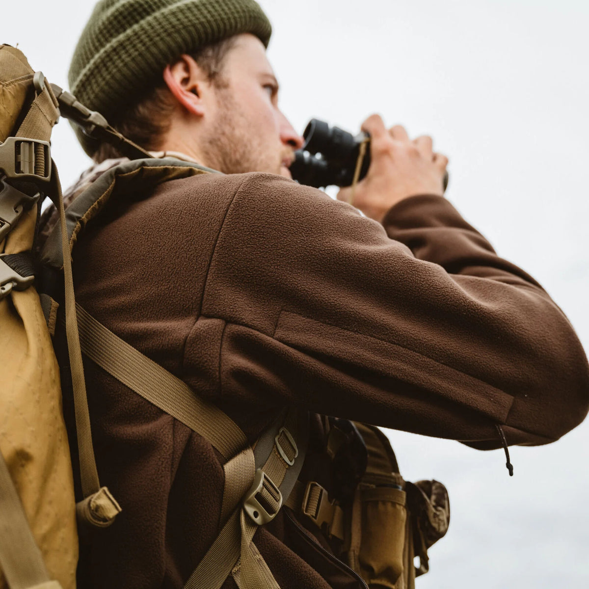 Brown textured fleece pullover worn by a person using binoculars, with a backpack visible.