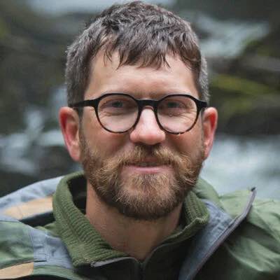 Black round eyeglasses on a man with a beard and green jacket.