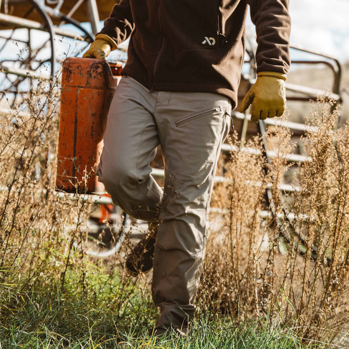 A person wears khaki pants with angled zippered thigh pockets while walking through dry brush.
