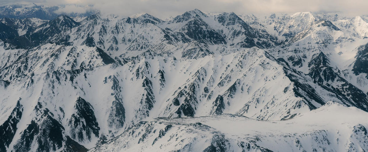 Snowy mountain range with jagged white peaks, dark rock, and cloudy sky.