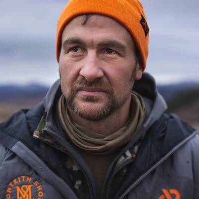 Man in orange beanie with black M-logo and gray jacket with Monteith Shops logo.