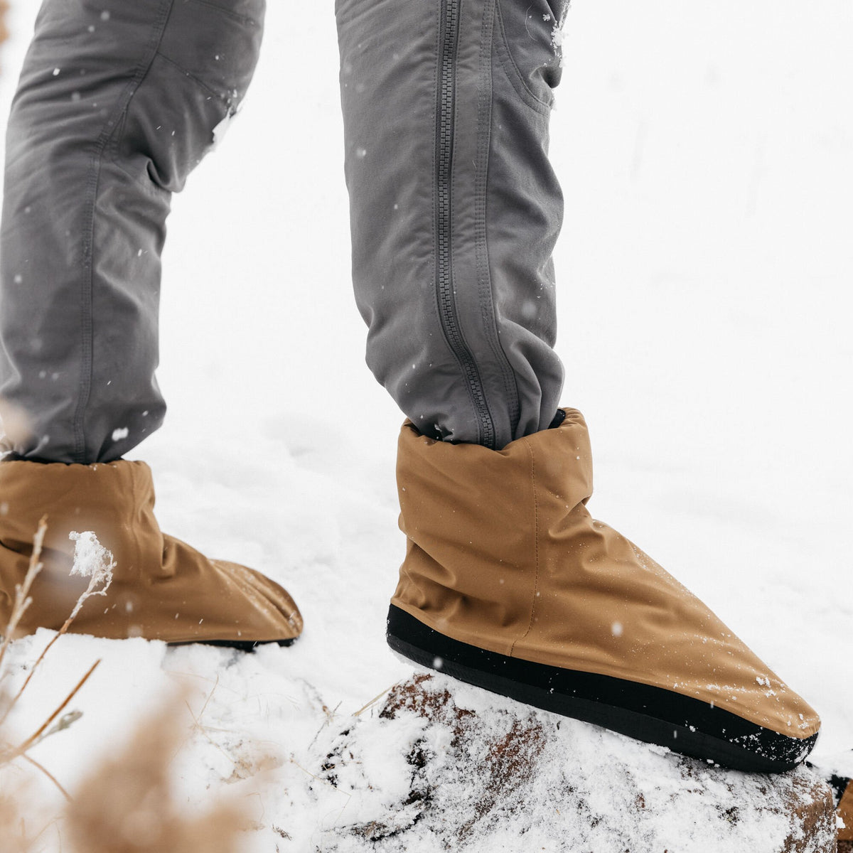 Tan insulated puffy boots with black soles, standing in light snow.