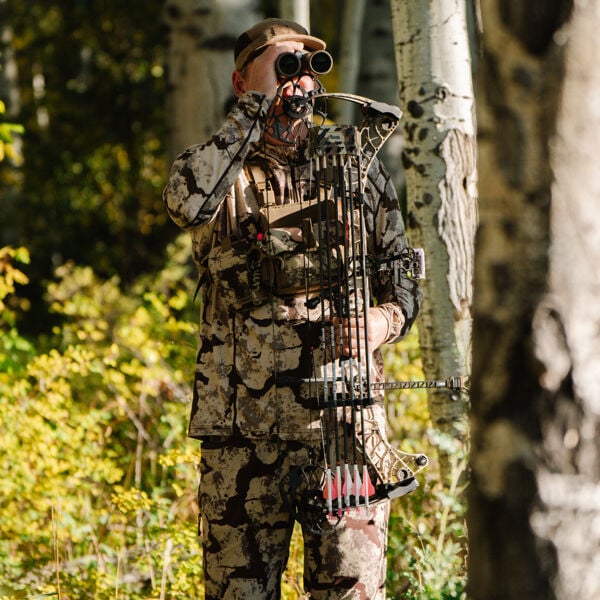 Light brown camo hunter with binoculars, holding a compound bow with arrows.