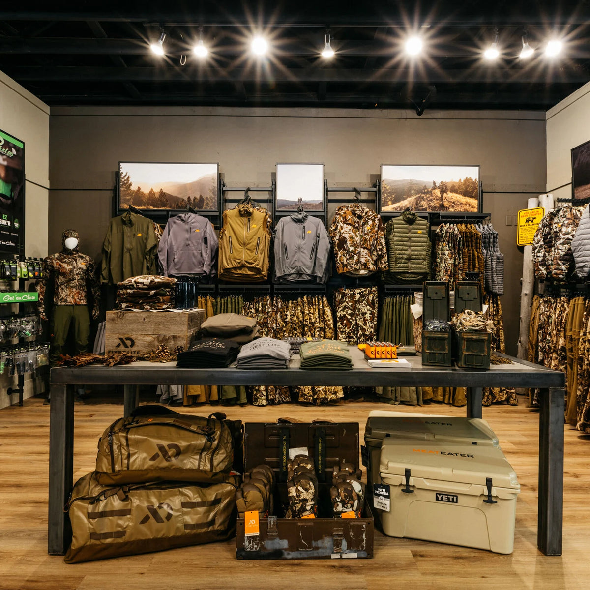 Hunting apparel store with camo clothing, green jackets, brown duffel bags, and a tan cooler.