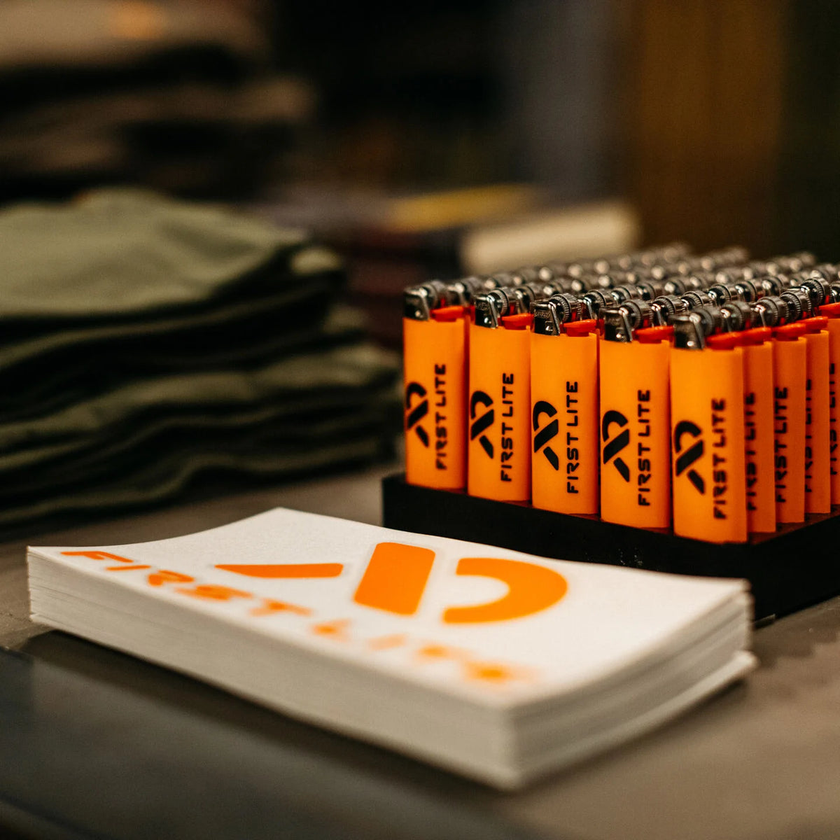 Orange First Lite lighters in a black tray, with a stack of white logo cards.