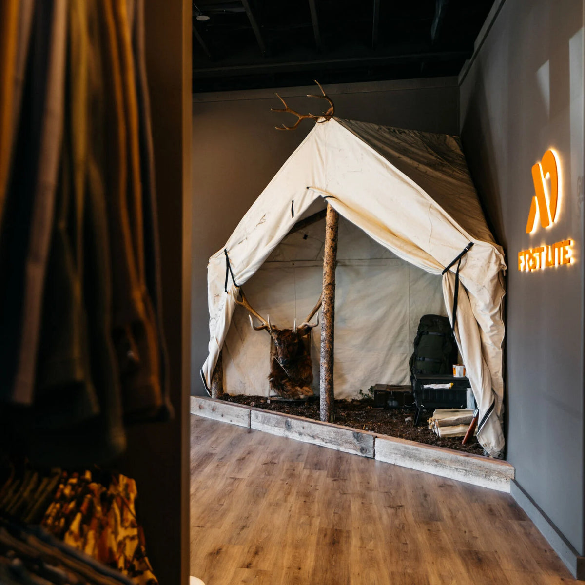 Beige canvas wall tent with antlered deer head, backpack, and firewood inside.