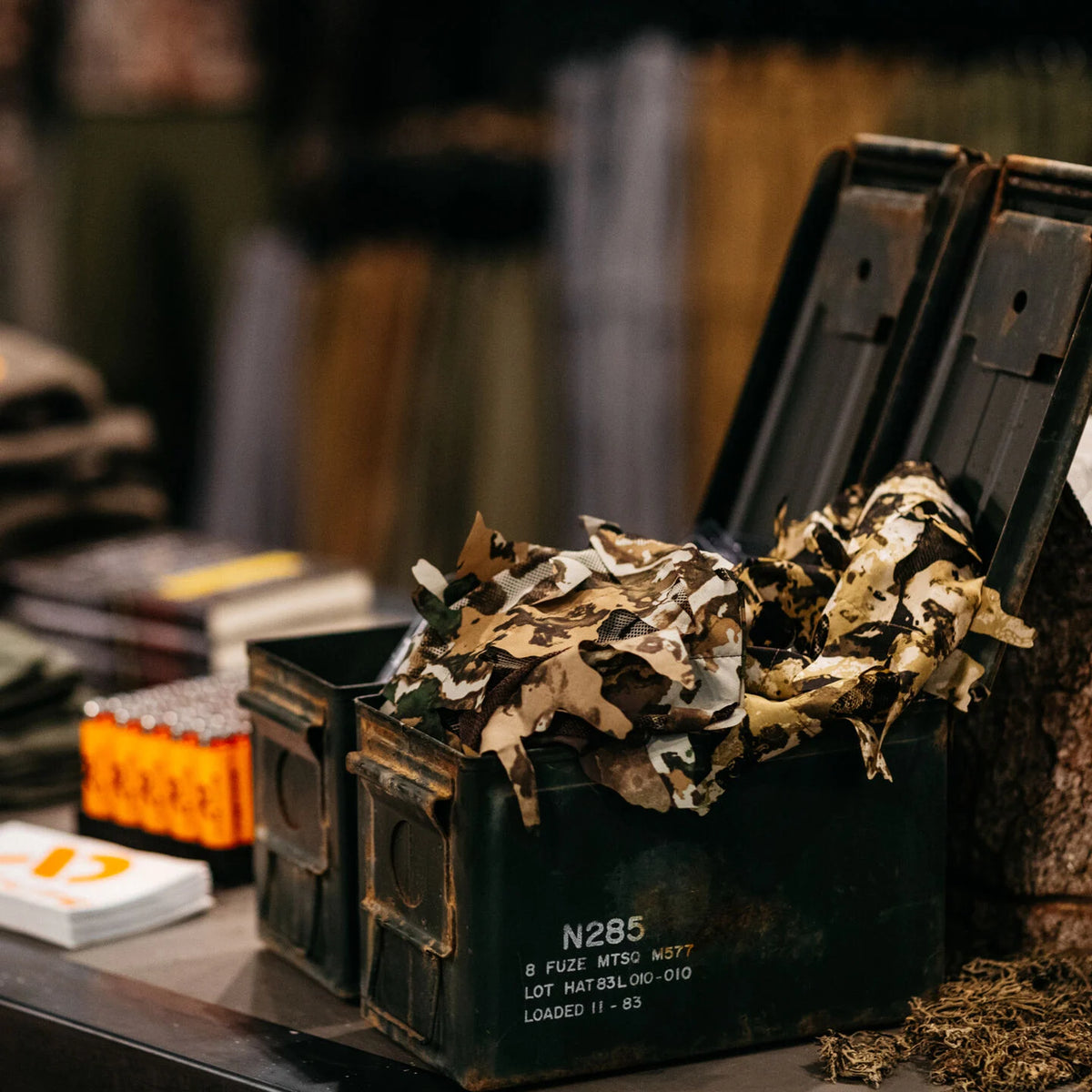Open, distressed dark green ammo box holding brown camouflage netting.