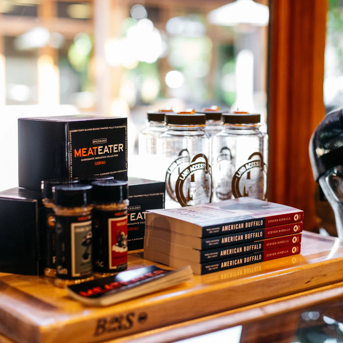 Black MeatEater spice boxes, red/black American Buffalo books, and clear Land Access bottles.