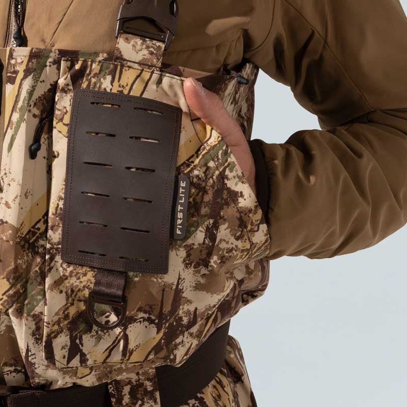 Camo hunting bibs with First Lite logo, brown patch with slits, and a hand in the pocket.