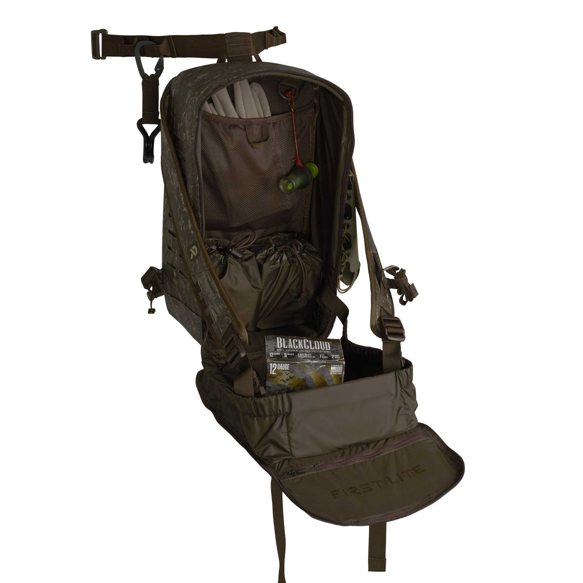 A dark camouflage First Lite hunting backpack is open, revealing internal storage including two drawstring pouches, a duck call, and a box of 12 gauge ammunition.
