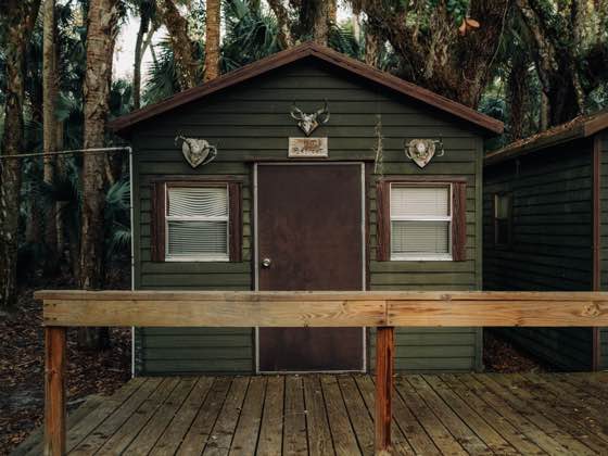 Dark green cabin with brown trim, decorative animal skulls, windows, and a wooden porch.