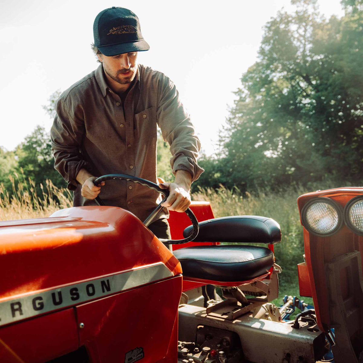 Man operating a red tractor in a field with trees in the background