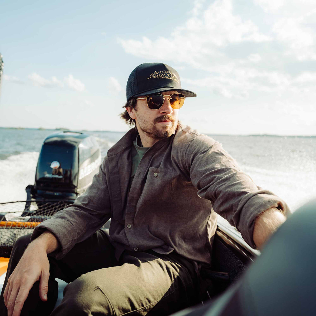 Man wearing sunglasses and a cap on a boat with water and sky in the background