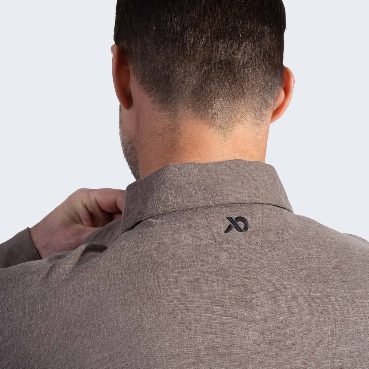 Man wearing a brown shirt with a logo on the collar against a light gray background