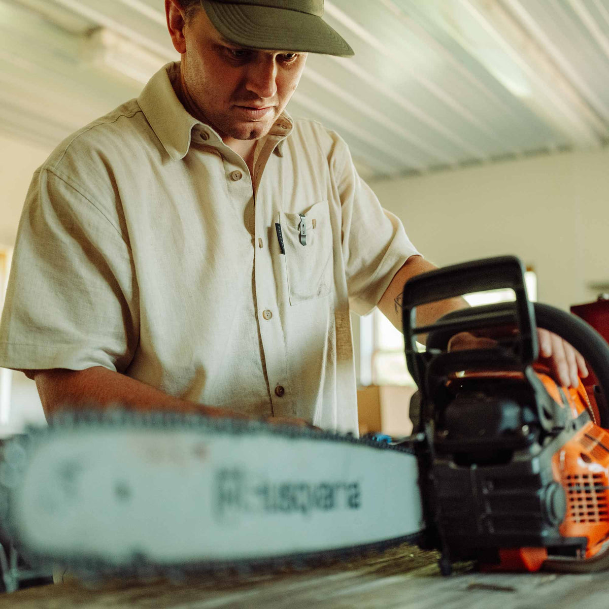 Man repairing a chainsaw wearing a sand button down shirt in a workshop