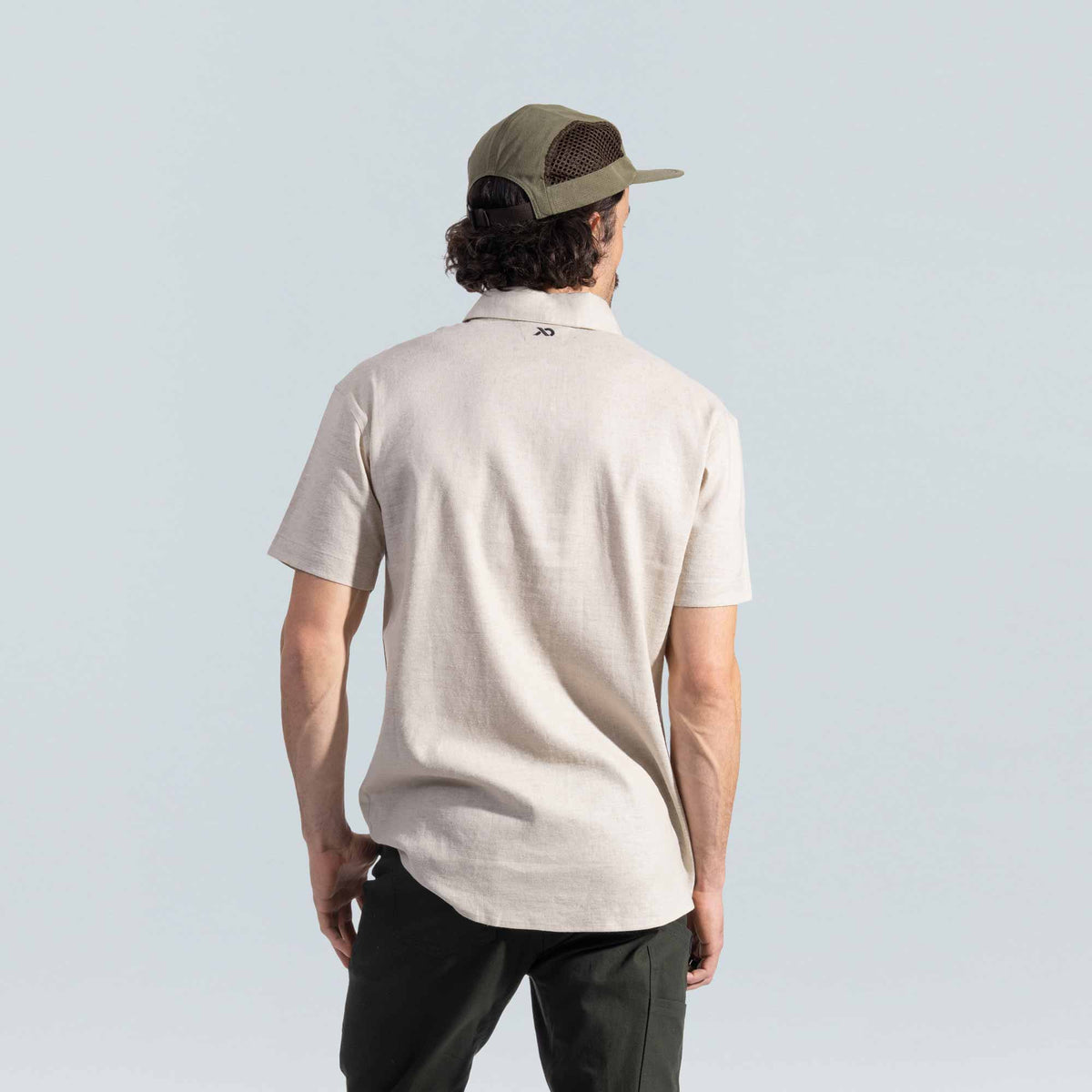Man wearing a beige button down shirt and green cap on a light gray background
