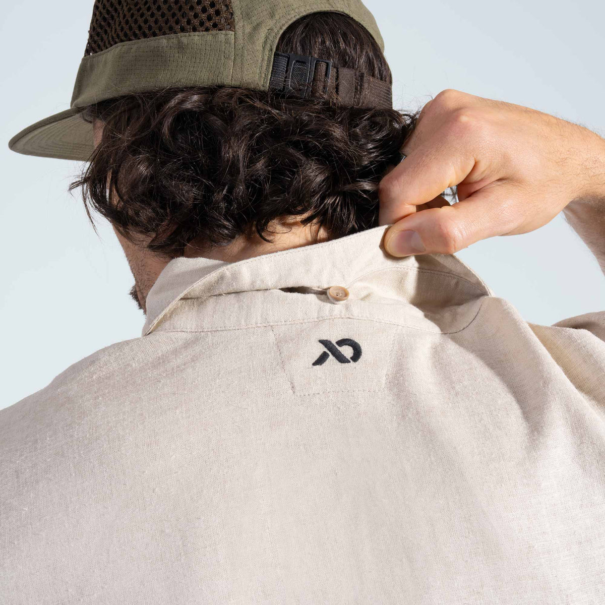 Person wearing a beige shirt with a First Lite logo, adjusting the collar against a white background.