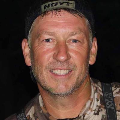 Black HOYT cap & camo FIRST LITE shirt worn by a smiling man.
