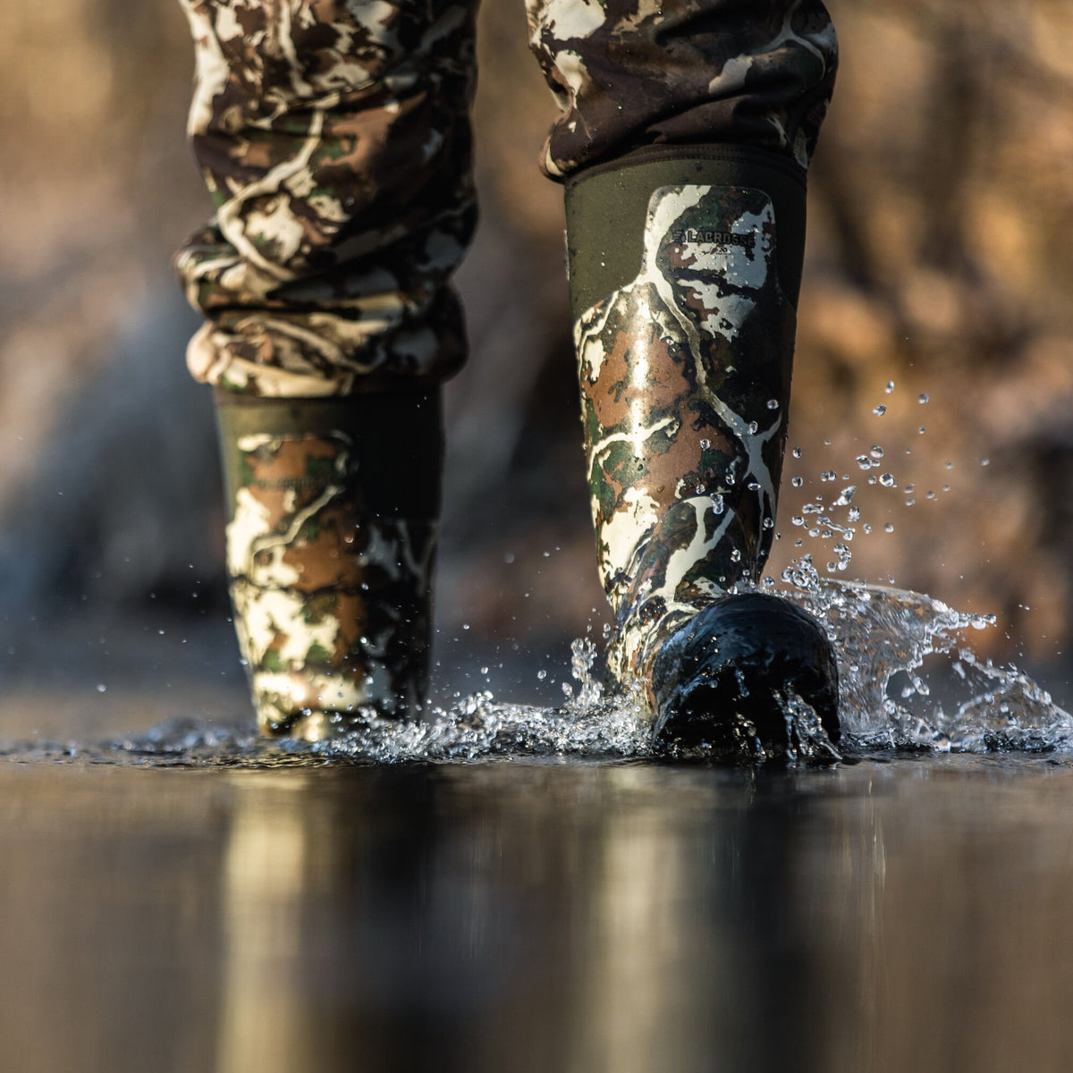 Tall LaCrosse camouflage rubber boots with matching pants splash in water.