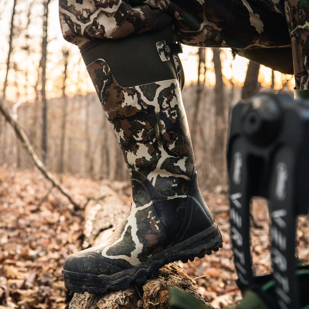 Knee-high LaCrosse hunting boot in white, brown, and green camouflage with a dark green adjustable cuff and a black lugged sole.