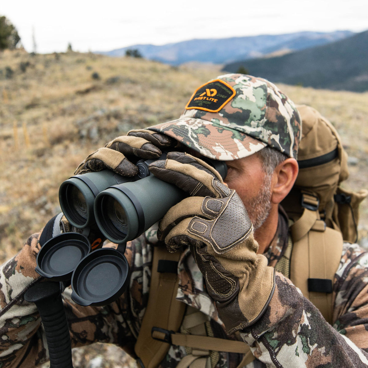 Dark olive binoculars with open black lens caps are held by tan gloved hands.
