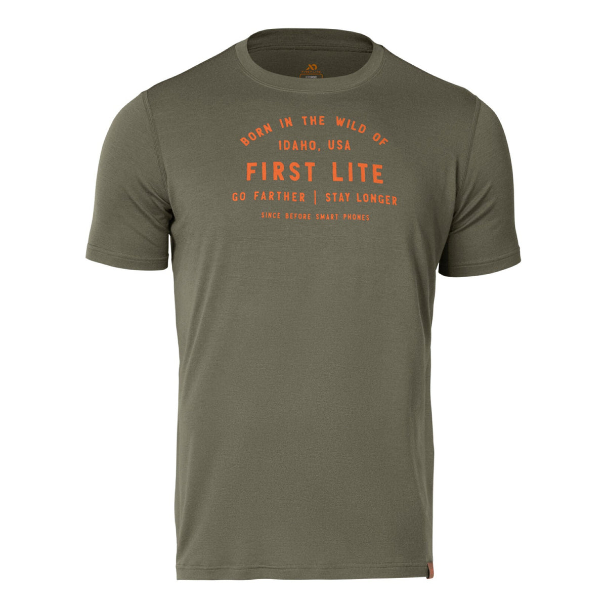 An olive green t-shirt features orange text on the front saying 'Born in the Wild of Idaho, USA First Lite Go Farther | Stay Longer Since Before Smart Phones' and a small brown tag on the lower right hem.