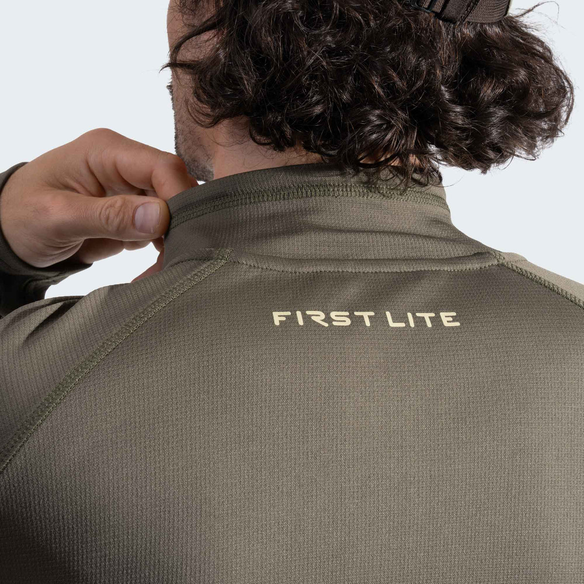 Person wearing a green quarter zip with 'First Lite' branding on a white background