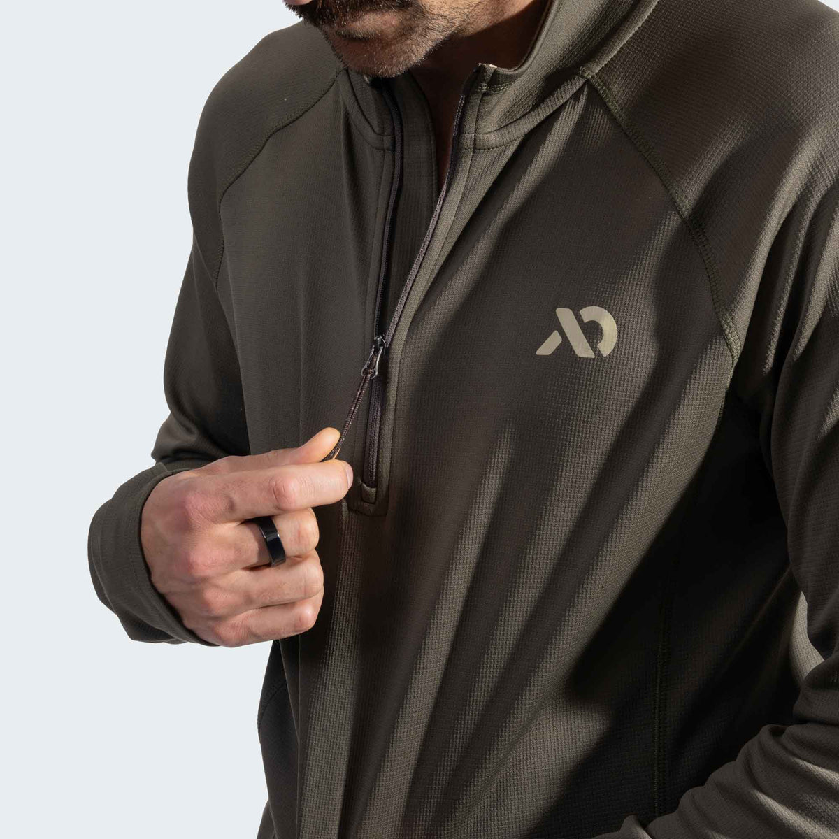 Person wearing a drab green quarter zip with athletic material and a First Lite logo and unzipped collar