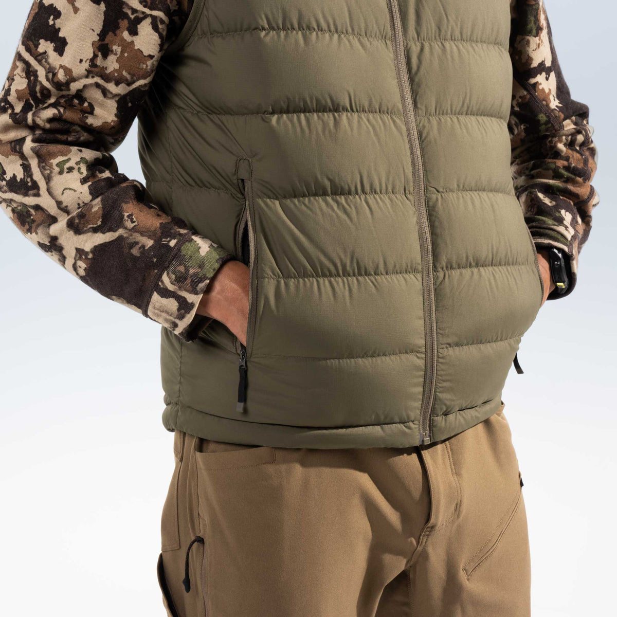 Close up of a man wearing a green puffer vest with his hands in his pockets. 