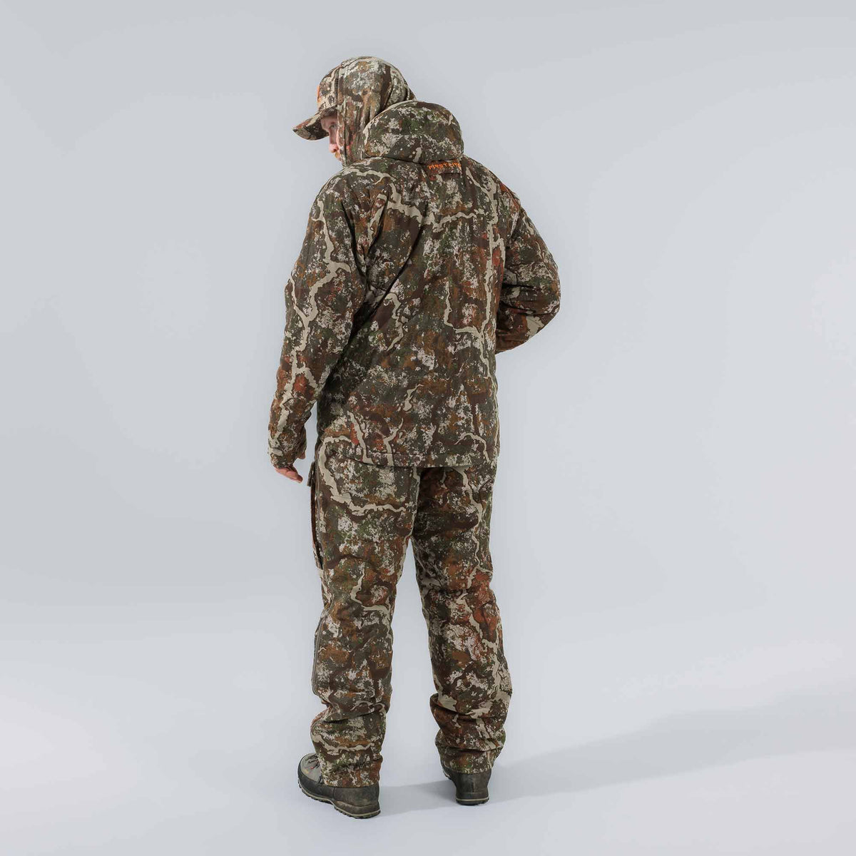 Man from behind wearing a full First Lite camouflage hunting suit with a hooded jacket, pants, and cap, featuring orange "FIRST LITE" text on the back.
