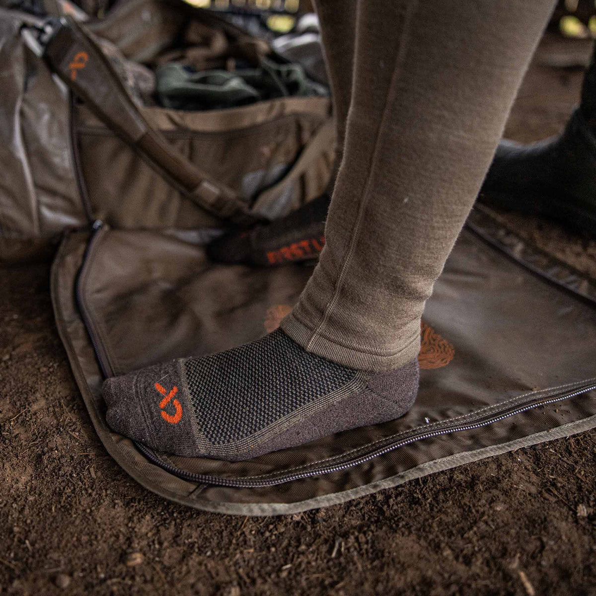 Dark grey sock with orange logo and textured knit on a foot, resting on a brown mat.