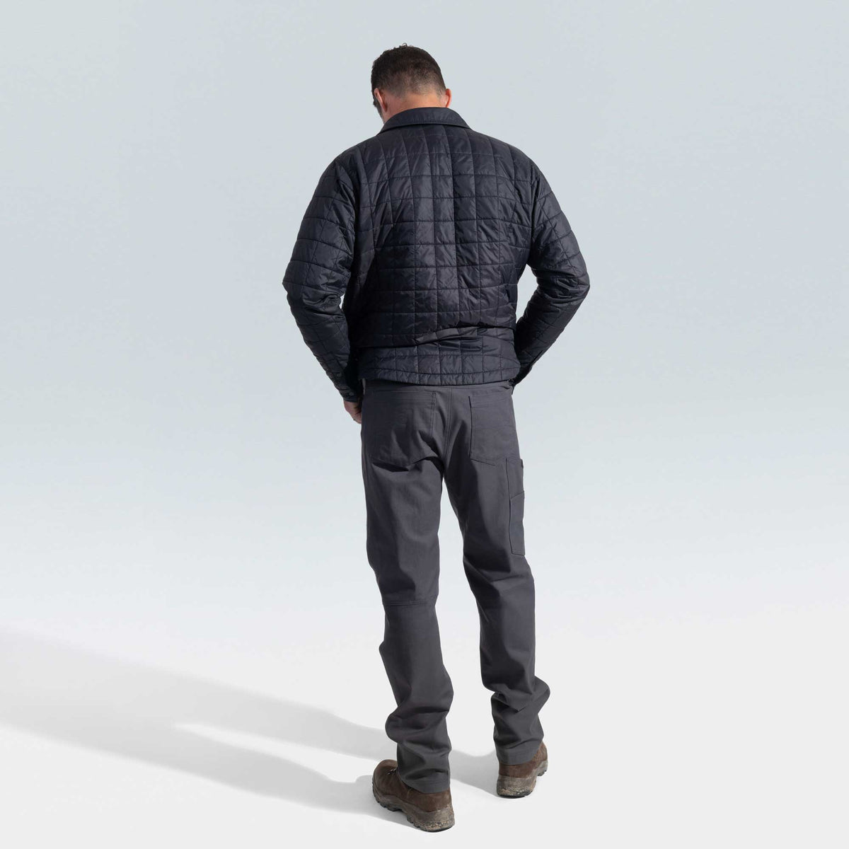 Man wearing a black quilted jacket and gray pants on a light gray background