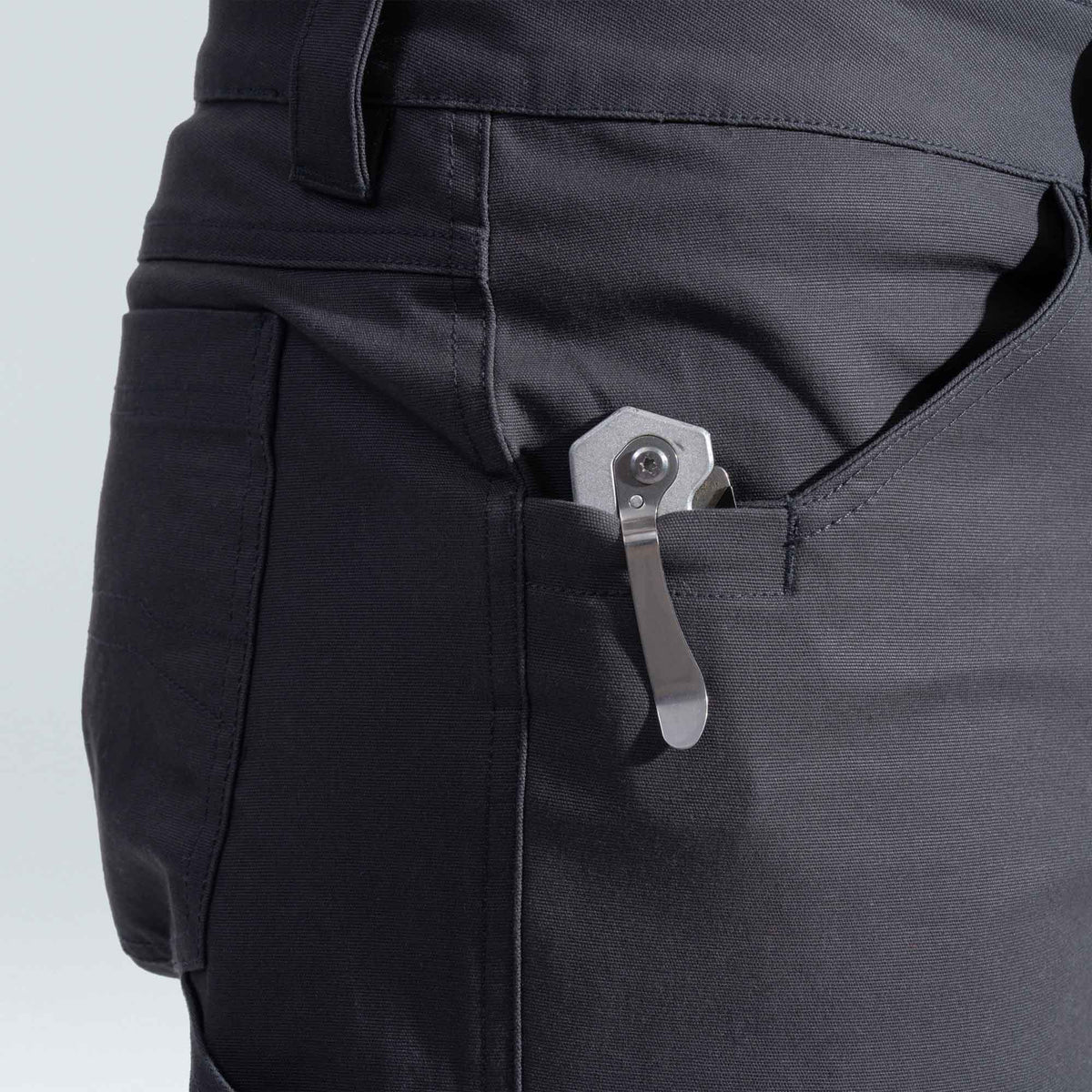 Close-up of black pants with a metal knife clip attached to the pocket on a light gray background