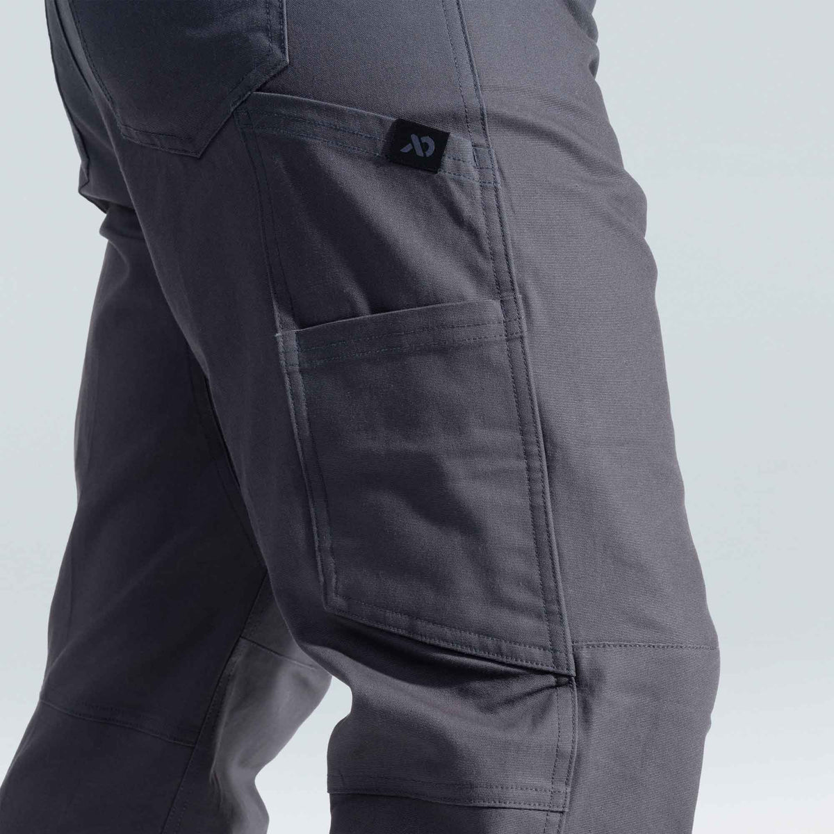 Close-up of dark gray pants with a First Lite logo on a light gray background