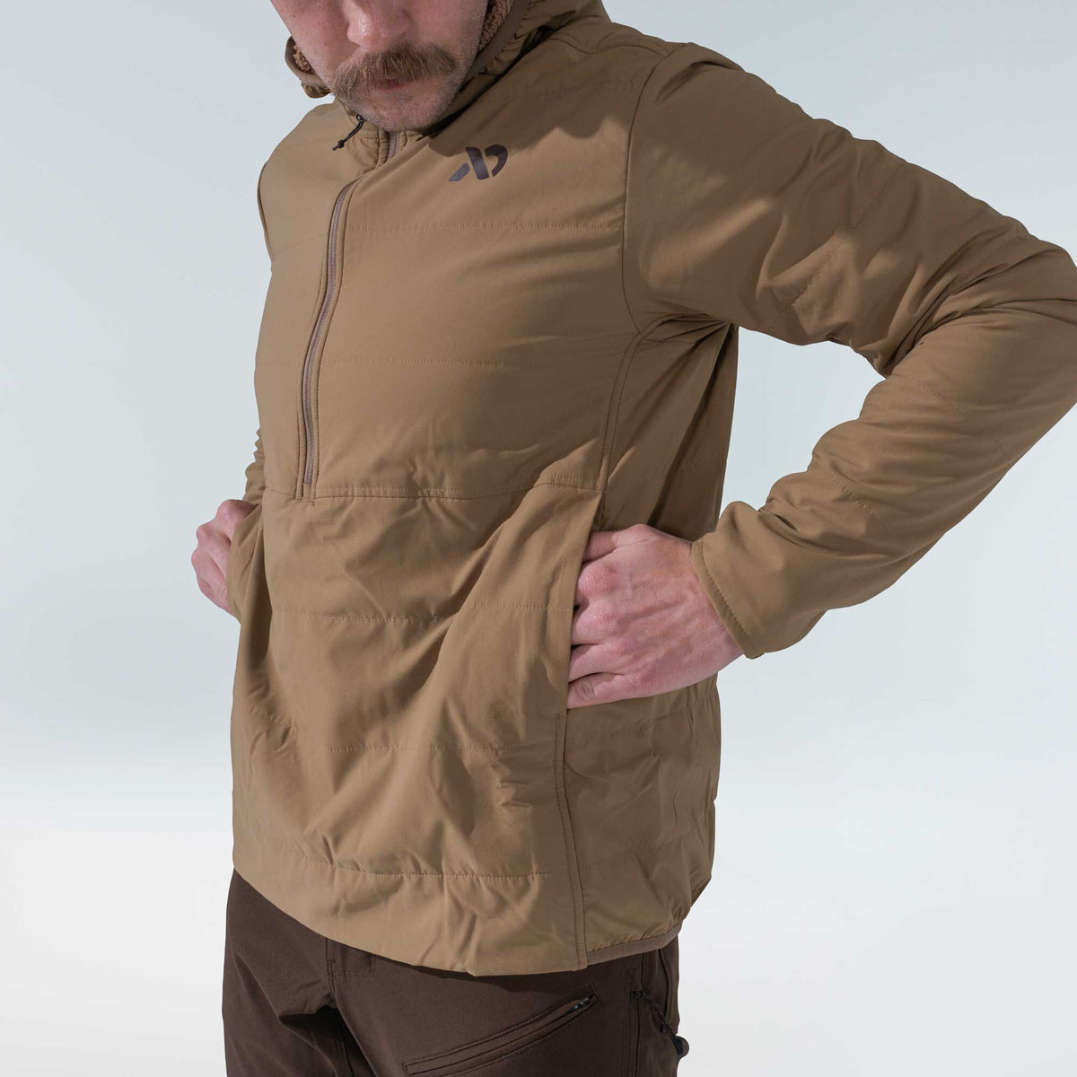 Tan hooded anorak jacket with a half-zip front, left chest logo, horizontal quilting, and side pockets.