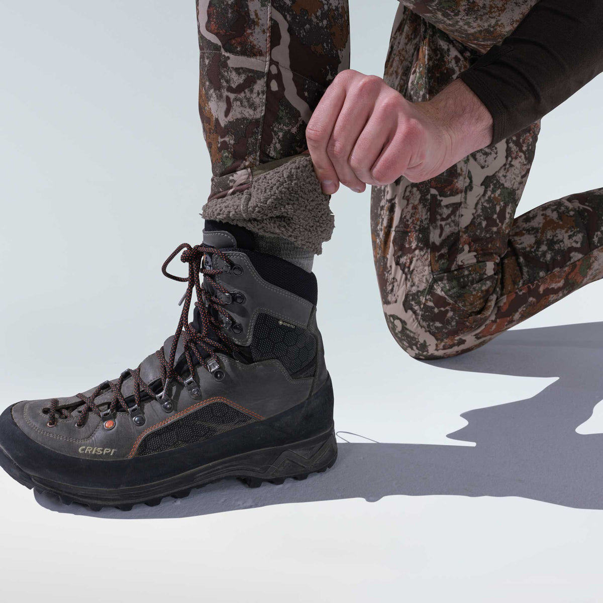 Dark grey Crispi GORE-TEX hiking boot with black accents and orange laces, worn by a person in camouflage pants.