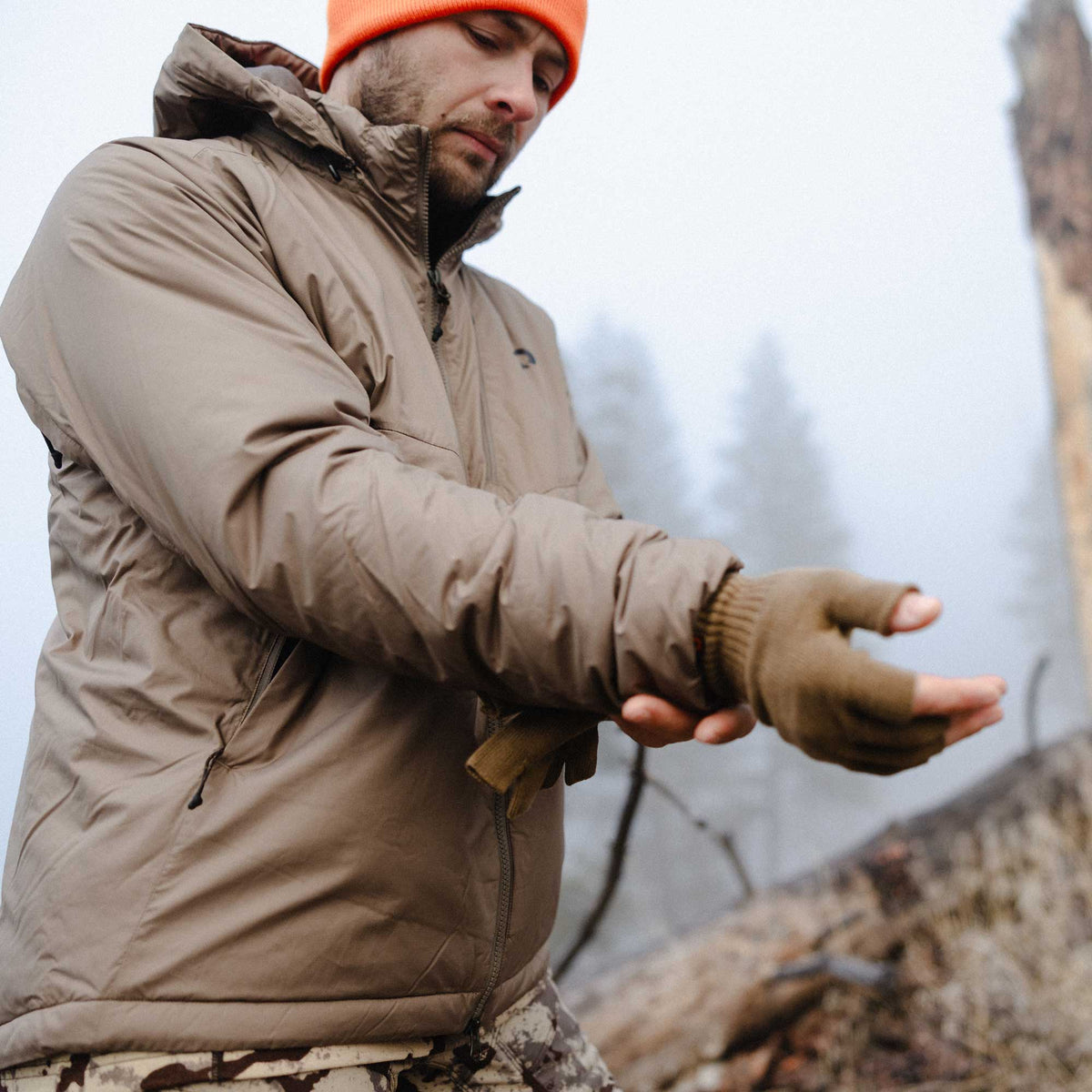 Brown hooded insulated jacket with zipper pockets worn by a man also wearing brown fingerless gloves.
