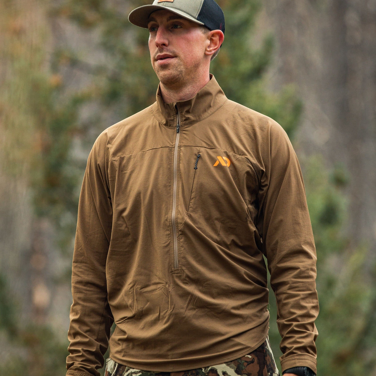 Man wearing a coyote brown textured quarter-zip pullover with an orange chest logo and a vertical zippered pocket.