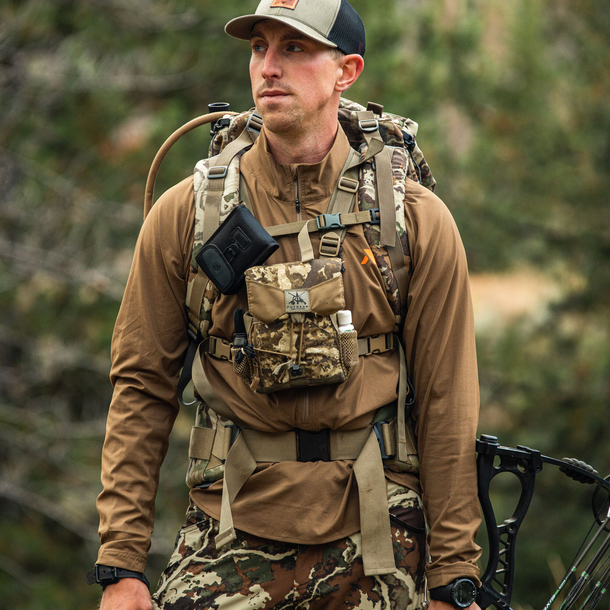 Man wears a brown quarter-zip long-sleeve shirt, camouflage backpack and chest rig with a rangefinder pouch and FHF Gear pouch, holding a compound bow.