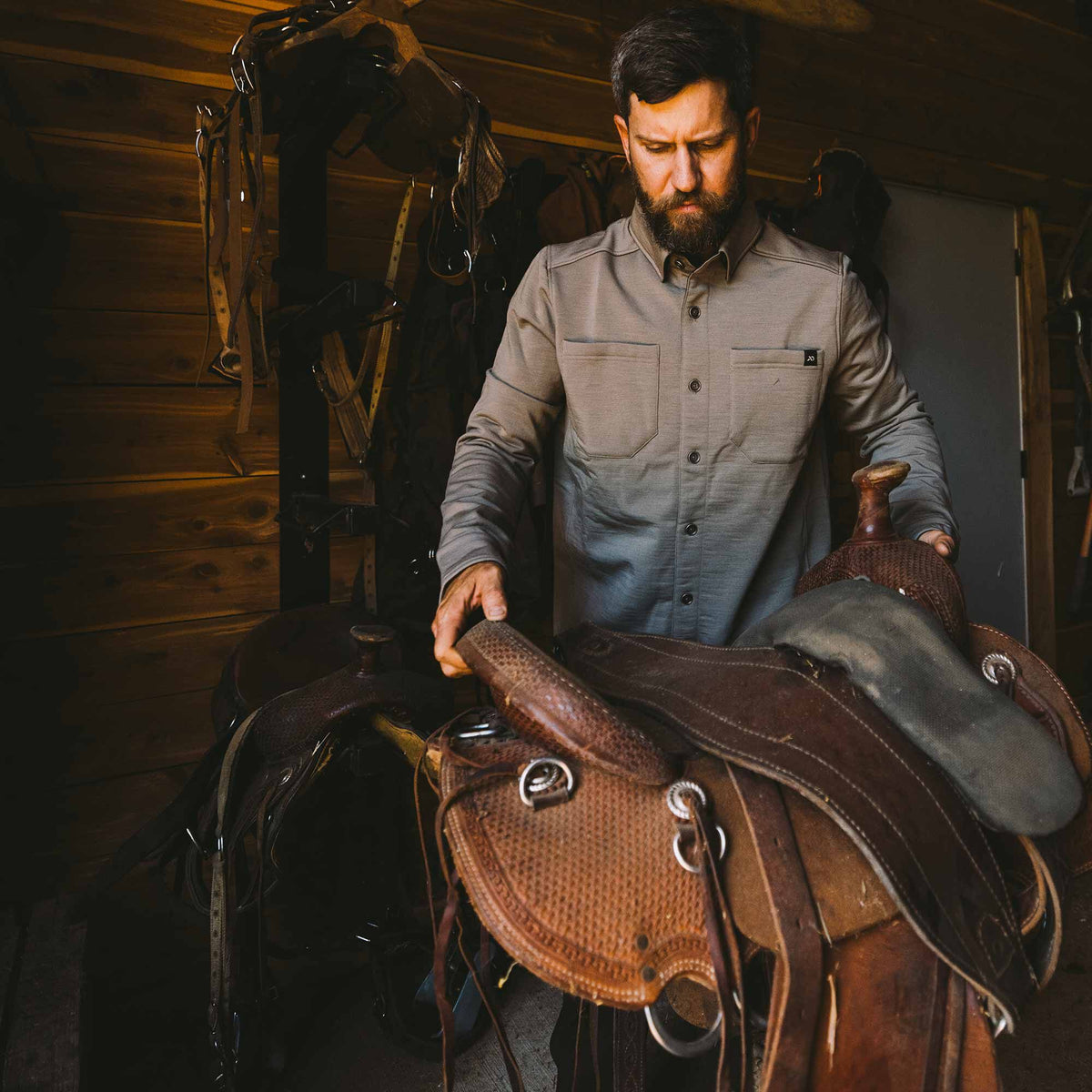 Taupe men's long-sleeve button-up shirt with a collar, dark front buttons, and two patch chest pockets, one featuring a small dark logo, worn by a man.
