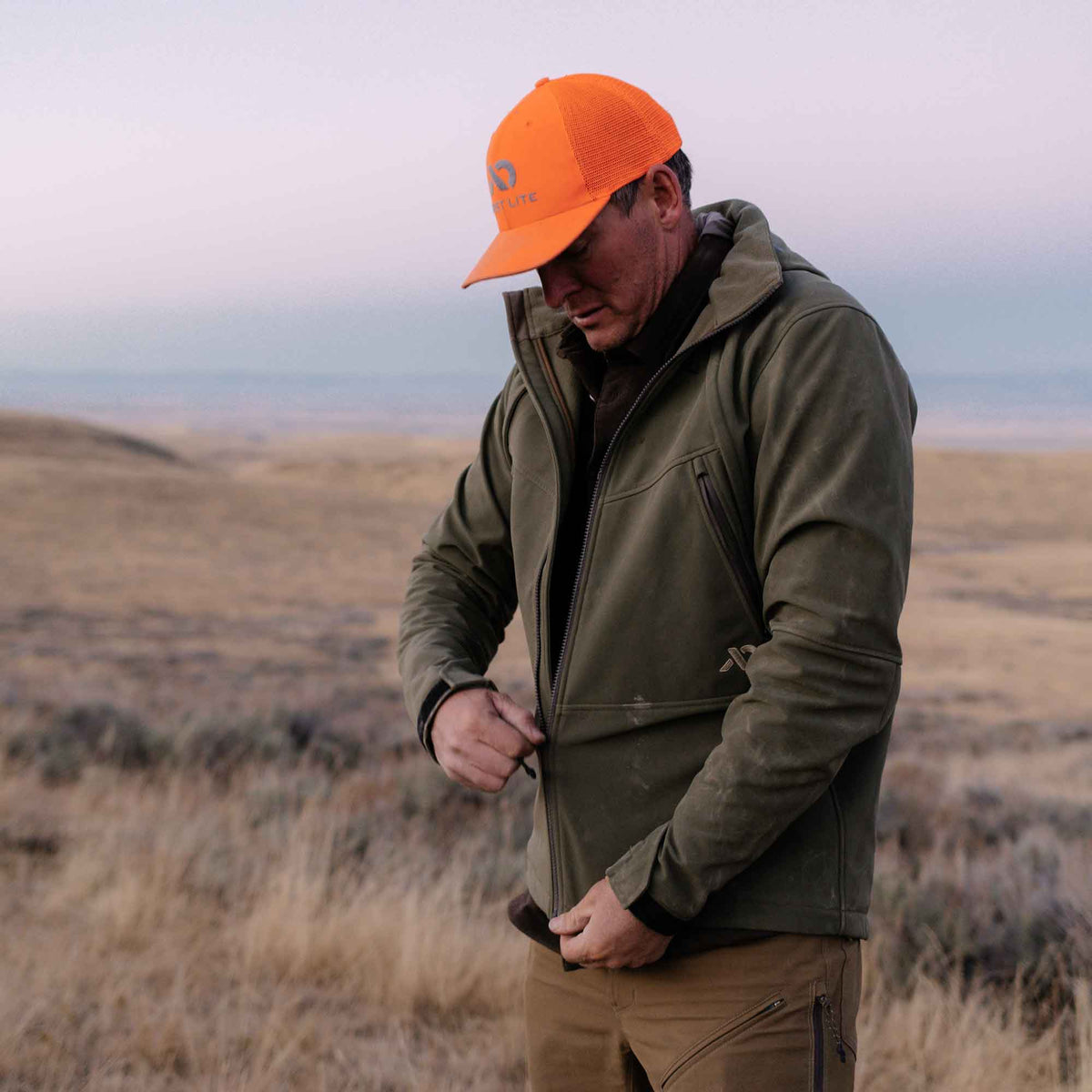 Olive green jacket with zippered chest pockets and adjustable cuffs, being zipped up by a man.