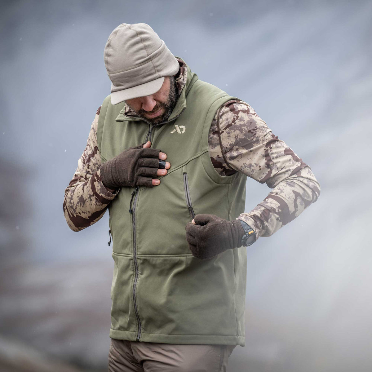 Sage green vest with a full front zipper, a chest logo, and zippered chest and hand pockets.