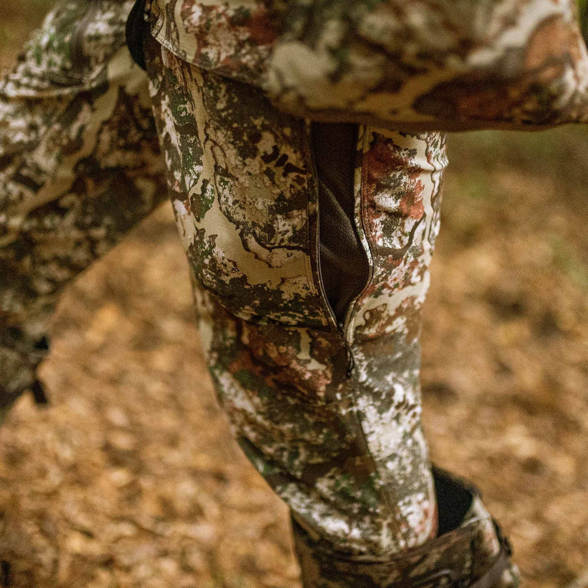 Camouflage hunting pants with an open side zipper revealing a dark mesh lining.