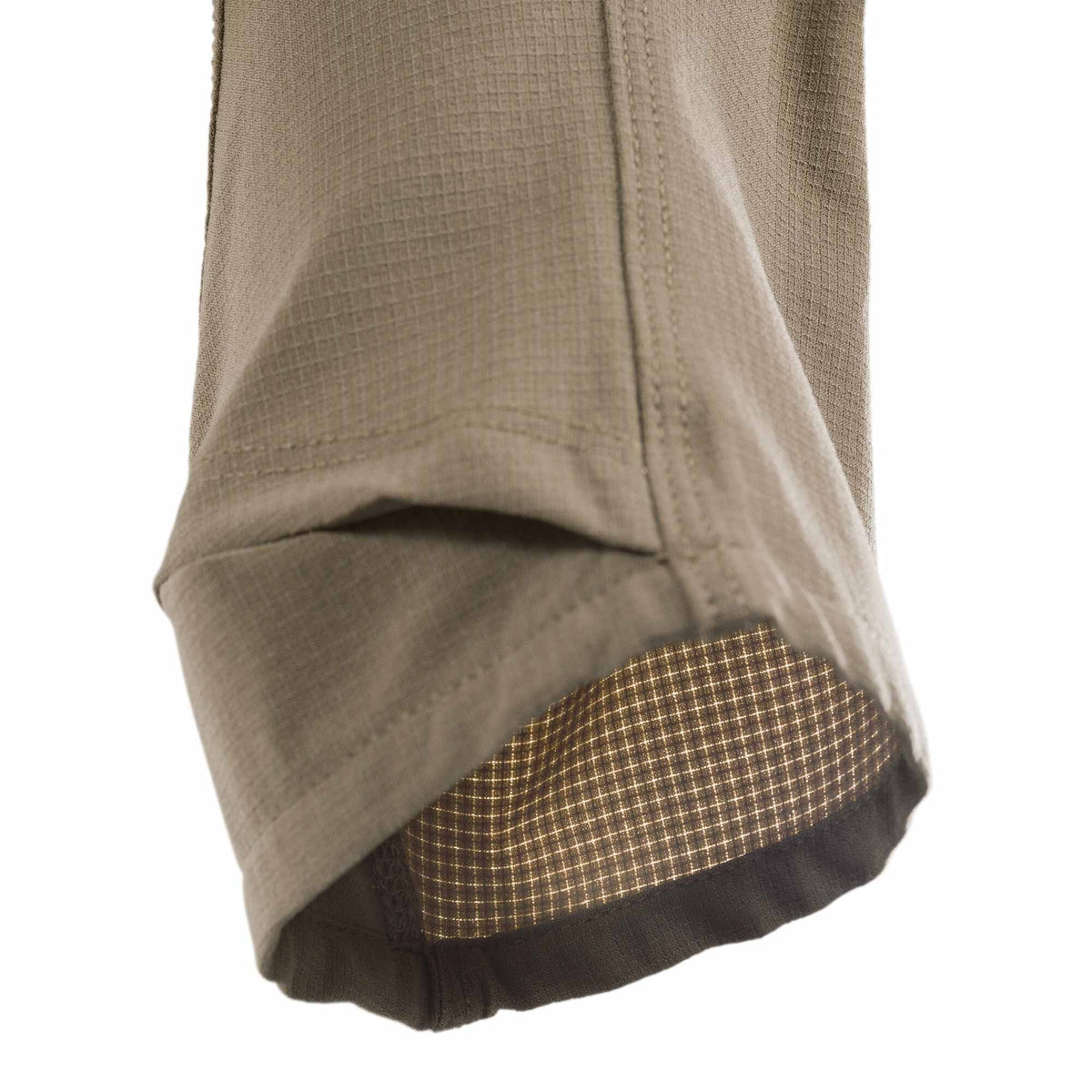 Close-up of a khaki ripstop pant leg, with the cuff folded to reveal a dark inner layer featuring a backlit grid pattern.