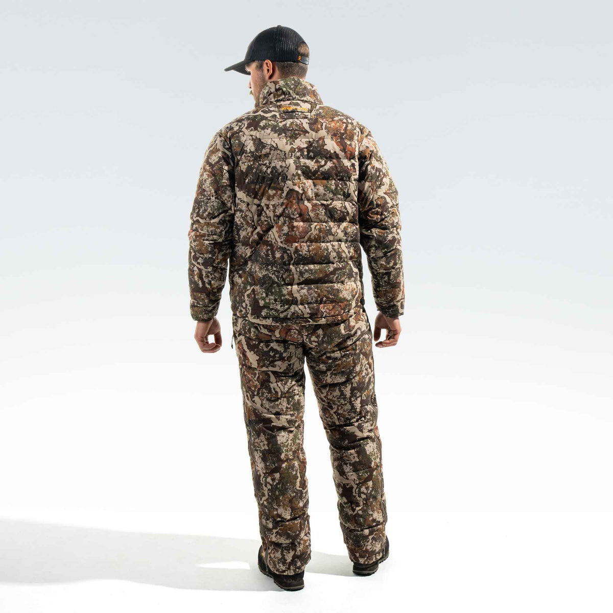 Behind shot of a man wearing a camo jacket and camo pants and a FIRST LITE black cap.