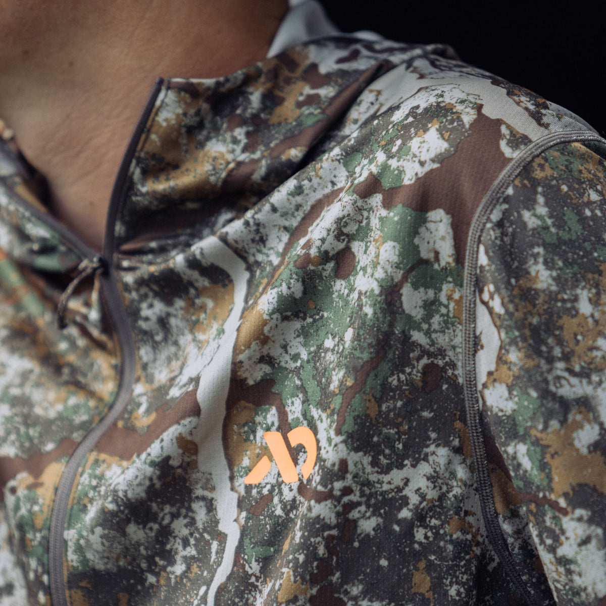 Camouflage hooded quarter-zip top with a gray zipper and an orange logo on the left chest.
