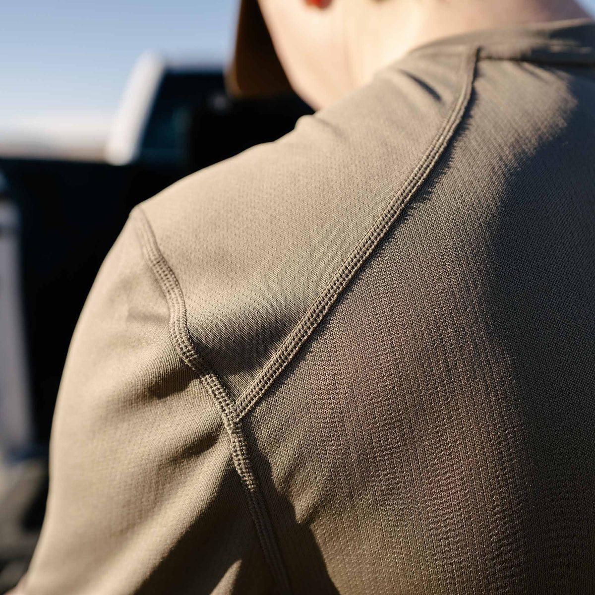Close-up of an olive green long-sleeve shirt showing flatlock seams on the shoulder and textured performance fabric.